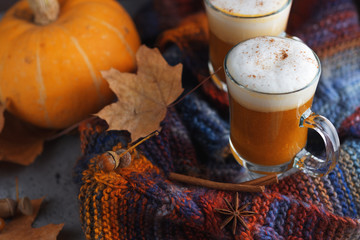 Pumpkin coffee latte. Autumn background with dry leaves and warm bright scarf . Home comfort hygge
