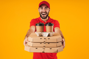 Portrait of unshaven delivery man in red uniform holding pizza boxes and takeaway coffee