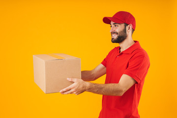 Image of pleased delivery man in red uniform smiling and holding packaging box