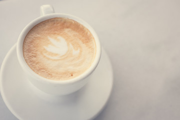 Cup of coffee with milk on marble table with wooden chairs in unfocused background, top view