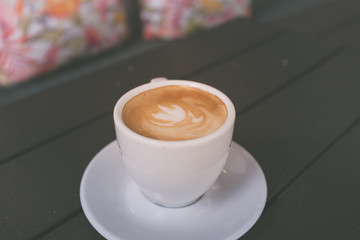 Cup of coffee on wooden table with colorful cushions in the background, vintage style