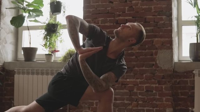Young man practice yoga pose at home with brick wall in slow motion. Healthy lifestyle concept. Attractive man doing yoga indoors