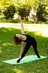 Woman practices yoga in morning in park in fresh air. Triangle pose.