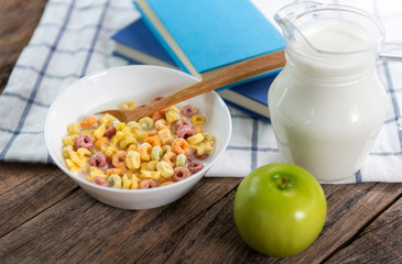 The colorful cereal rings in bowl with milk and green apple on the wooden table,concept dieting, healthy food and eating.