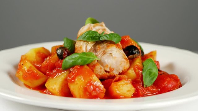 Traditionally prepared cod in Spanish. Served in tomato sauce with boiled potatoes, olives and basil. Front view.  Food presentation. Turning the platter.