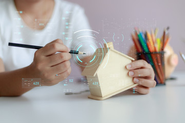 Happy Asian woman using pencil to draw with wooden house piggy bank and Cyber technology HUD GUI...