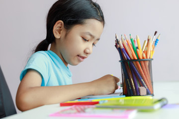 Little asian girl putting doing homework use color pencil to draw on paper select focus shallow depth of field