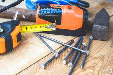 An old hammer with nails and a yellow ruler of roulette near glasses for eye protection and a laser level on a blackboard background. Tools for construction work.