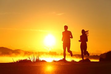 Fototapeta na wymiar Couple shilouette running at sunrise on the beach