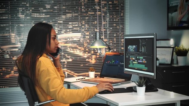 Multiracial video and sound editor speaking with somebody by smartphone and mounting video on modern software