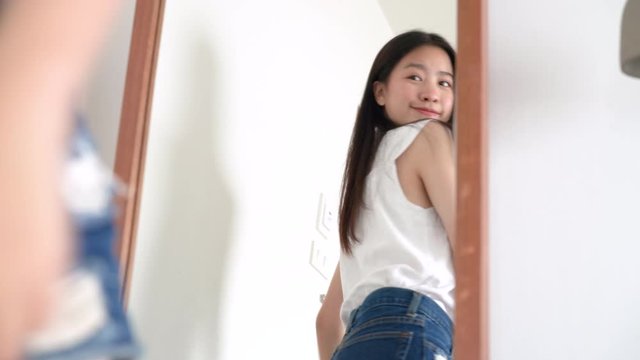 Young beautiful asian woman look at mirror after wear clothes her checking body for ready next travel trip on summer in hotel room 4k resolution.