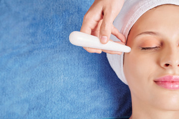 Close-up image of beautician using quartz stick to massage area around eyes and get rid of undereye...