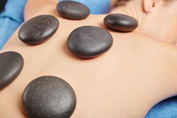 Smooth heated basalt stones on back of young female spa salon client, selective focus