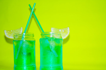  Refreshing blue cocktail drink with lemon slices on the sides of a glass and drinking tubes on a bright yellow background