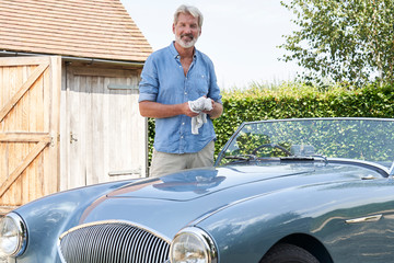 Portrait Of Mature Man Restoring Classic Sports Car Outdoors At Home