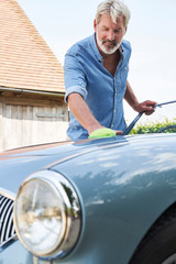 Mature Man Polishing Restored Classic Sports Car Outdoors At Home
