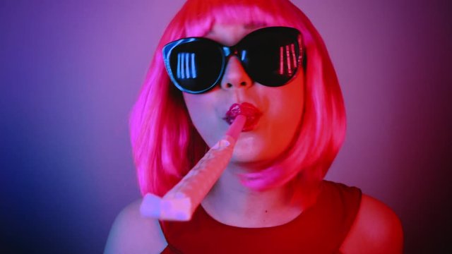 Woman in a bright pink wig at a party. She is blowing at a party horn. Birthday Celebration.
