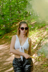 Fototapeta na wymiar Young woman in sunglasses and summer clothes using smoke bomb