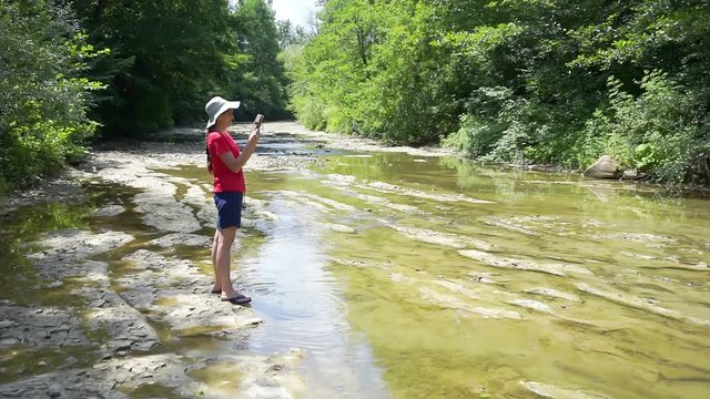 walks in the wild on a sunny summer day.young woman on a walk on the shore of a mountain river.girl takes pictures of the surrounding space on a modern electronic device.