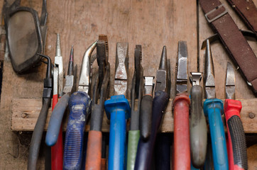 a set of colored different pliers hanging on the workplace in the workshop