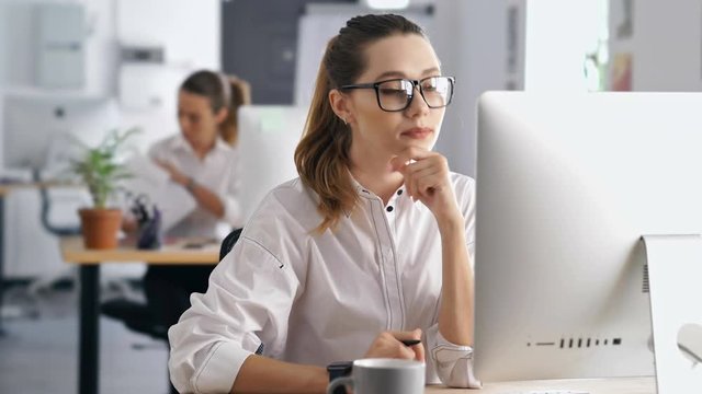 Young displeased concentrated woman working in office using pc computer looking at documents of her colleague
