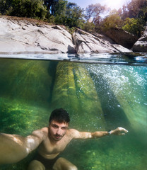 An adult guy diving deep in the mountain river and taken his selfie with a half underwater camera....