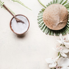 Fototapeta na wymiar Coconut oil or butter in wooden bowl with spoon and whole coconut on tropical leaves and flowers, top view . Copy space . Healthy plant based fat source. Vegan food and cosmetic
