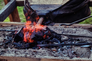 Bellows inflate the fire in the coals. Blacksmith heats iron for forging.