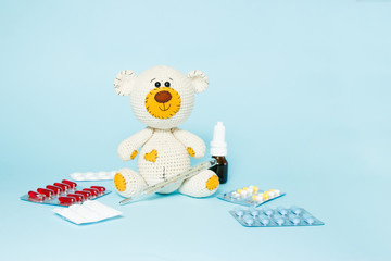 Children's knitted toy teddy bear with pills takes the temperature of a mercury glass thermometer on blue background. Child' disease concept