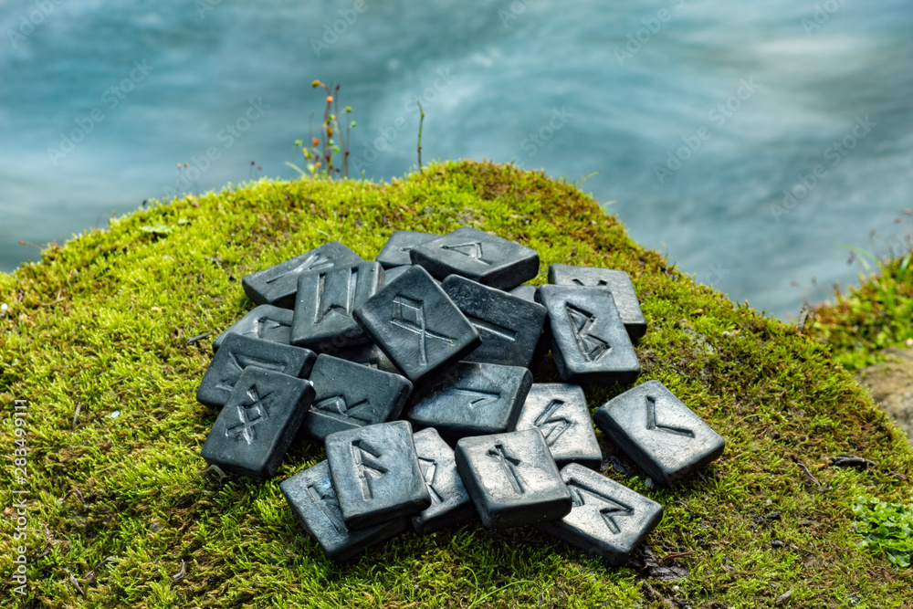 Wall mural 24 norse runes on the green grass and the evening river background