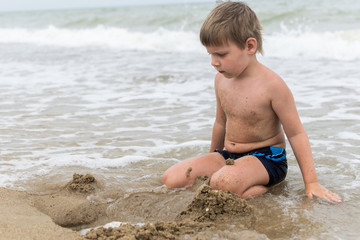 A little boy builds from sand on the seashore, the ocean. Baby is played on the beach.