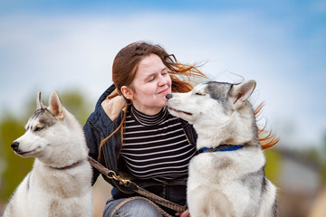 Young beautiful girl with red hair is sitting on a pier with two husky dogs. Woman with a pair of Siberian Husky © voltgroup