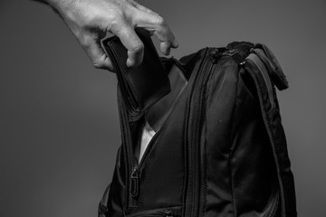 Black and white photo of a thief's hand pulling a purse from a backpack on a gray background