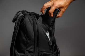 Thief's hand pulls a purse from a backpack on a gray background