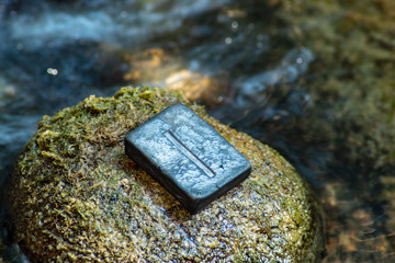Norse rune Isa on the stone and the evening river background. Calmness, stability or delay, stagnation.