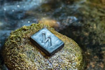 Norse rune Sowilo on the stone and the evening river background. The sun, energy, protection from dark forces.