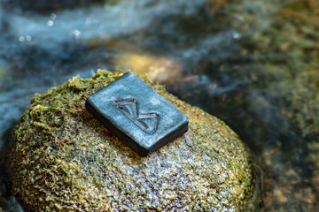 Norse rune Bercana on the stone and the evening river background. Birch, femininity, motherly care and protection. The rune is associated with the Scandinavian Goddess Frigg.