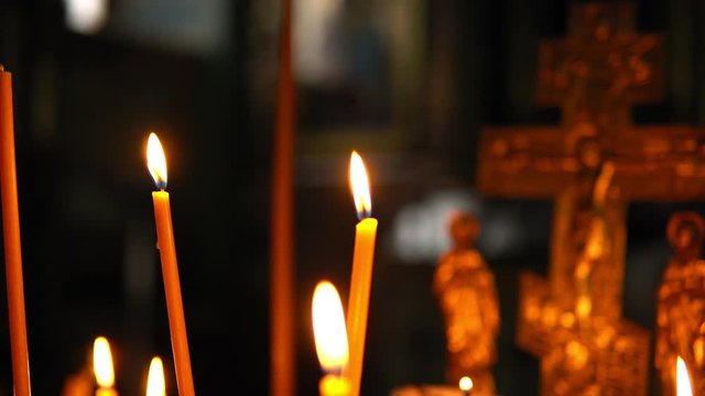 Burning candles close-up against the blurred Golden crucifixion of Jesus Christ in a dark room of the Orthodox Church, smooth focus on the subject
