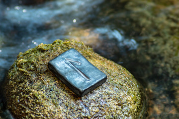 Norse rune Laguz (Laukr) on the stone and the evening river background. Love, youth, intuition, mysticism, magic. Water, flow, life.