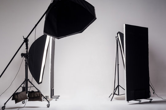 Professional photo studio with light setup included octagon softbox on boom, strip soft box and reflector on light gray background.