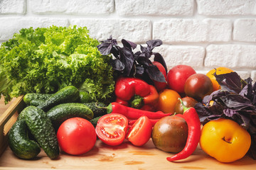 Various vegetables and salad leaves.in a wooden box on the kitchen table against the background of a white brick wall. Close-up, copy space.