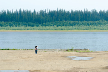 Girl traveler goes to the edge of the pier on the shore, holding her hair to the river vilyu with spruce forests and the tundra of Yakutia in the Far North of Russia.