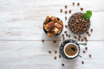 Cup of coffee, coffee beans and fresh dates on white wooden background