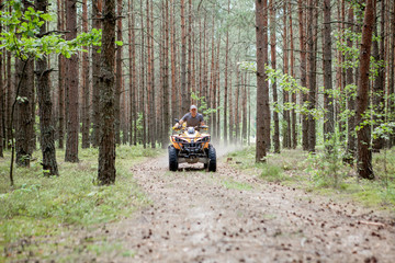 Man riding a yellow quad ATV all terrain vehicle on a sandy forest. Extreme sport motion, adventure, tourist attraction.