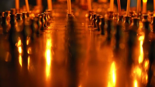 Large gold candleholder with a variety of cells for candles and blurred a little gold crucifix, the camera slowly pans on burning candles close-up