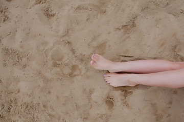 Woman tanned legs, straw hat and bag on sand beach. Travel concept. Relaxing at a beach, with your feet on the sand.