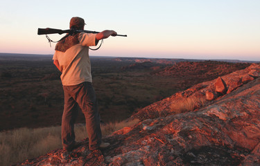 Hunter with  rifle on his shoulder looking down the mountain