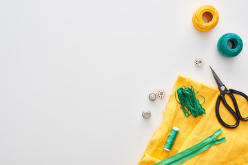 top view of zipper, scissors, thimbles, threads, knitting yarn balls, bobbins, fabric on white background
