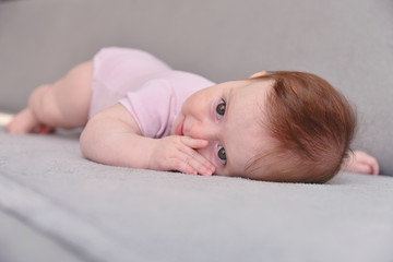 Happy Three Month Old Baby on White Background. Baby girl lying on her stomach on a grey background.