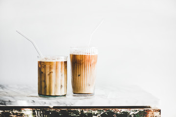 Homemade iced latte coffee in glasses with straws on grey marble table, white wall at background, copy space. Summer cold refreshing drink concept - obrazy, fototapety, plakaty